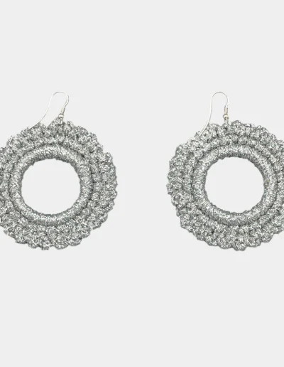 Mujer luciendo pendientes de círculo tejidos a crochet en hilo plateado, diseño artesanal y bohemio, ideales para looks únicos y elegantes