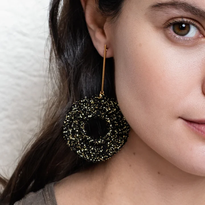 Modelo con pendientes de ganchillo hechos a mano en hilo negro brillante, diseño circular con barra dorada, Pendientes Aurora Boreal de BeMeknes.