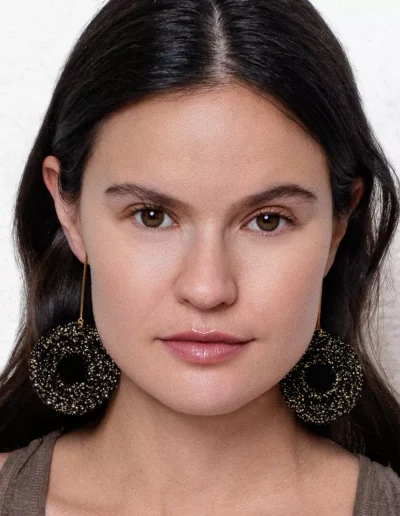 Modelo con pendientes de ganchillo hechos a mano en hilo negro brillante, diseño circular con barra dorada, Pendientes Aurora Boreal de BeMeknes.