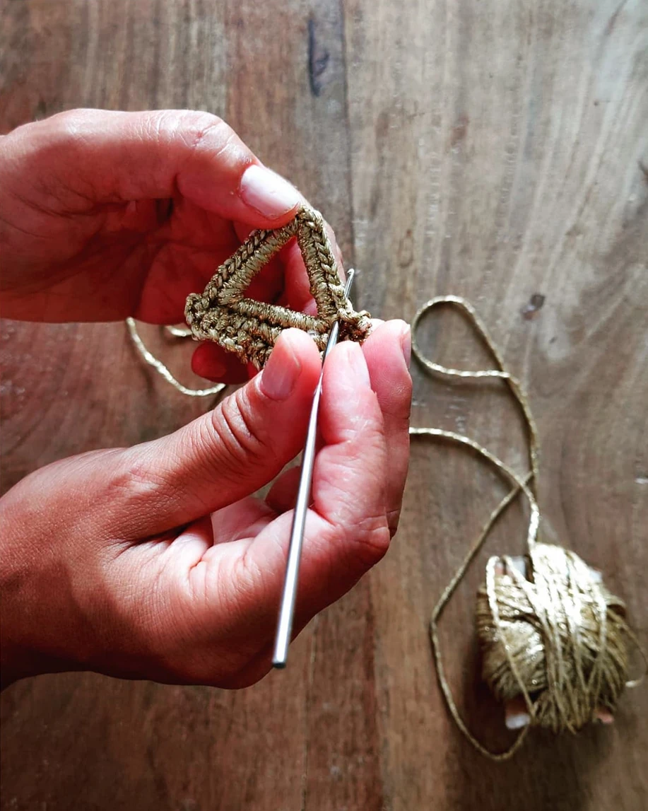 Manos artesana tejiendo crochet con hilo dorado