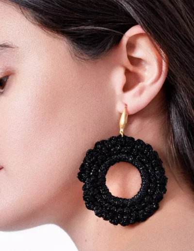 Close-up lateral de mujer con pendientes de círculo negro tejidos a crochet, donde se aprecia la textura artesanal del hilo y el diseño ligero. Ideal para looks urbanos con toque handmade.