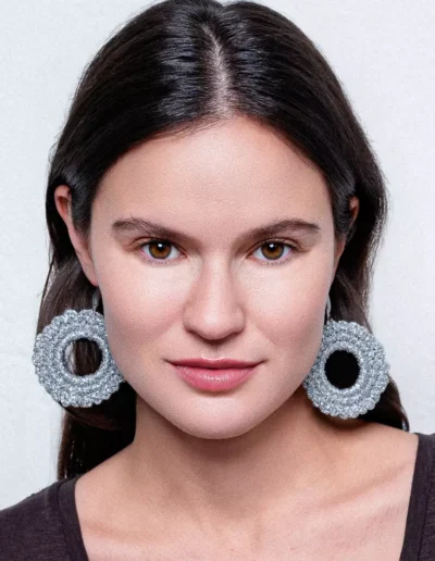 Pendientes circulares plateados de crochet artesanal BeMeknes - los pendientes que no pesan. Primer plano de mujer sonriente luciendo esta joyería textil en tono oro, donde se aprecia la textura handmade y el brillo delicado. Piezas slow fashion elaboradas con ganchillo, símbolo de diseño circular (unidad y eternidad). Ideales para looks boho-chic o minimalistas, combinan ligereza y artesanía. BeMeknes: bisutería ética, hecha a mano para quienes valoran detalles con significado.