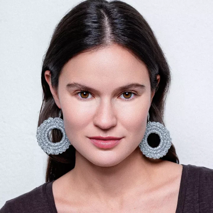 Pendientes circulares plateados de crochet artesanal BeMeknes - los pendientes que no pesan. Primer plano de mujer sonriente luciendo esta joyería textil en tono oro, donde se aprecia la textura handmade y el brillo delicado. Piezas slow fashion elaboradas con ganchillo, símbolo de diseño circular (unidad y eternidad). Ideales para looks boho-chic o minimalistas, combinan ligereza y artesanía. BeMeknes: bisutería ética, hecha a mano para quienes valoran detalles con significado.