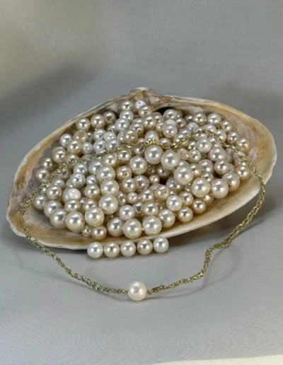 Collar Reina Margot perla blanca colocado sobre concha marina con perlas de río, joyería textil artesanal