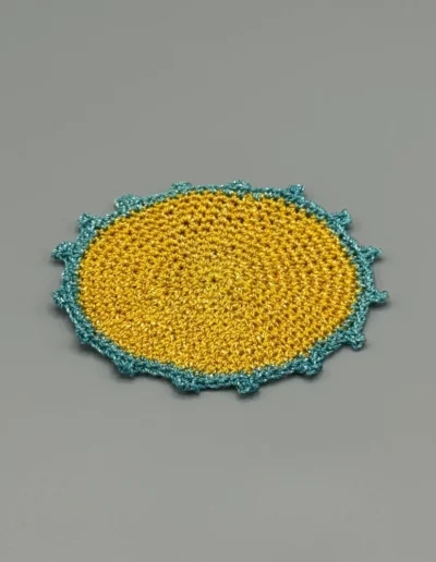 Detalle del posavaso artesanal amarillo con puntilla esmeralda.
