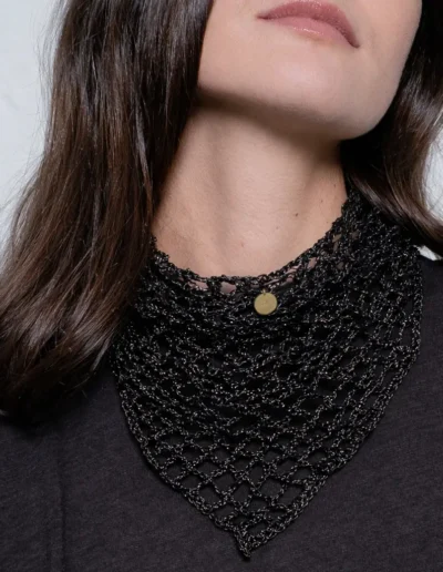 Modelo llevando pañuelo triangular de crochet negro con hilo dorado, detalle del cuello